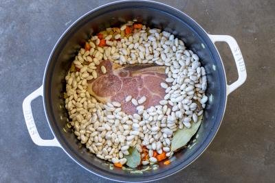 Beans and ham added to veggies in a pot.