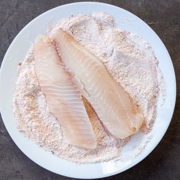 Tilapia coating in a seasoning on a plate.
