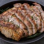 Sliced pork shoulder in a baking pan with herbs.