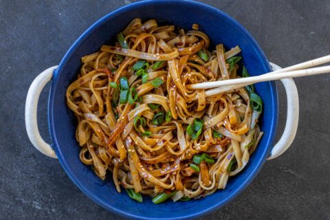 Noodles with green onions and chopsticks in a bowl.