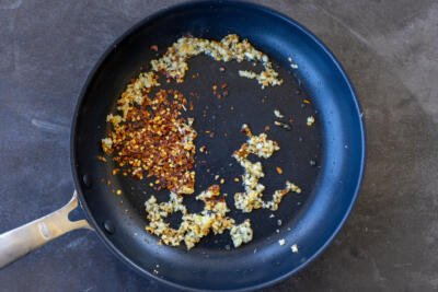 Red pepper flakes cooking in a frying pan with garlic.
