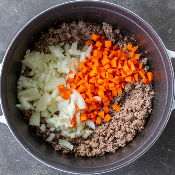 Veggies added to cooked ground meat in a pot.