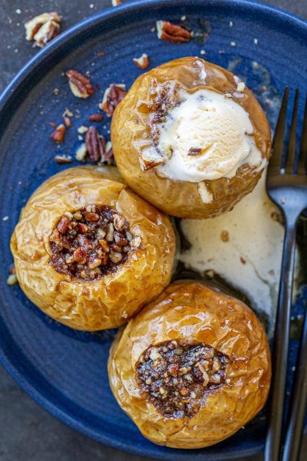 Utensils on a plate with baked apples and toppings. 