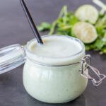 Creamy Tomatillo Dressing in a jar with a spoon and herbs around.