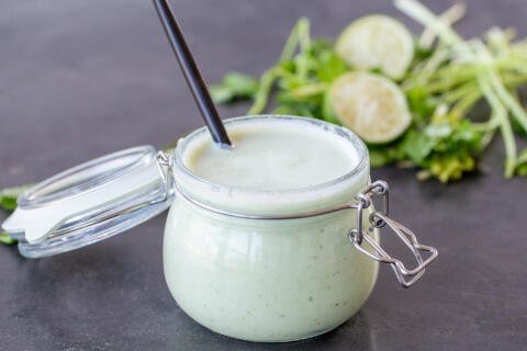 Creamy Tomatillo Dressing in a jar with a spoon and herbs around.