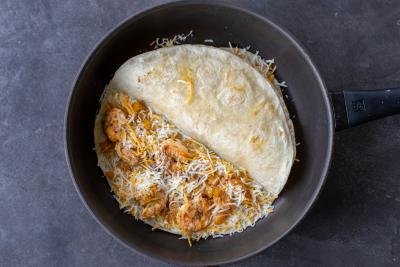 Shrimp and cheese added to tortilla in a pan.