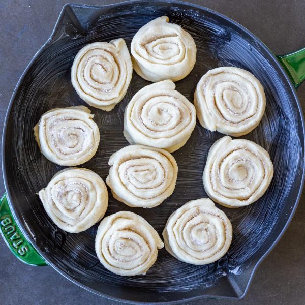 Raw cinnamon rolls on a buttered pan.