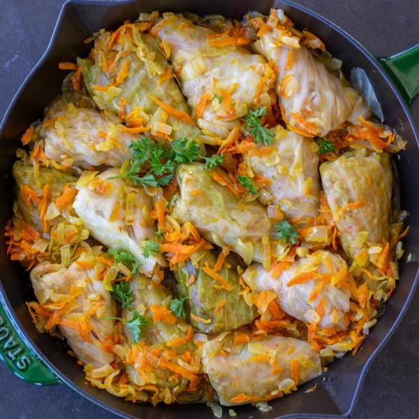 Vegetarian cabbage rolls in a pan with veggies and herbs.