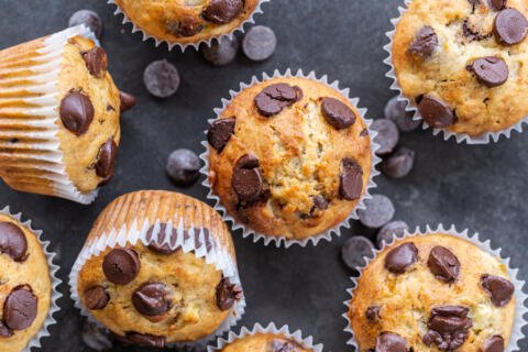A pile of Banana Chocolate Chip Muffins with chocolate around.