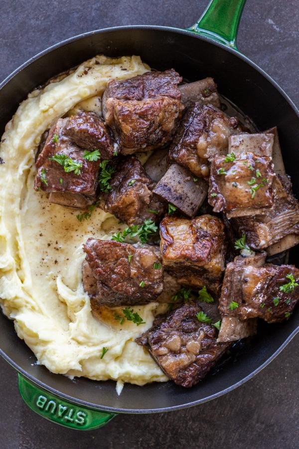 Slow cooker short ribs in a pan with side and herbs. 