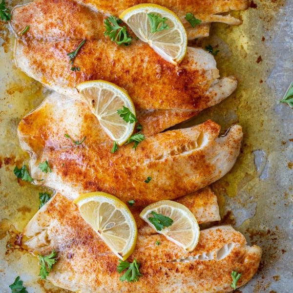 Baked tilapia on a sheet pan with lemon and herbs.