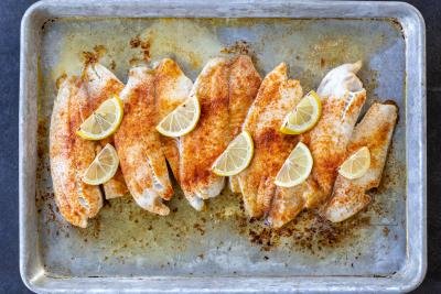 Baked tilapia on a baking pan with lemons.