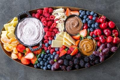 Board with fruits, cheese and dipping sauce.