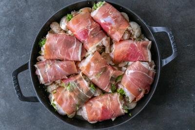 Chicken wrapped in prosciutto in a pan.