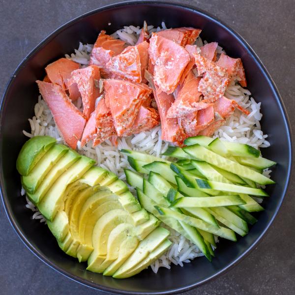 Rice in a bowl with salmon, avocado and cucumbers.