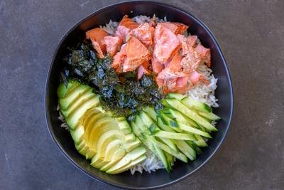 Rice in a bowl with salmon, avocado, seaweed and cucumbers.