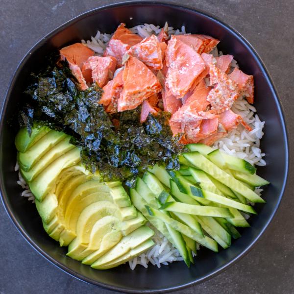Rice in a bowl with salmon, avocado, seaweed and cucumbers.
