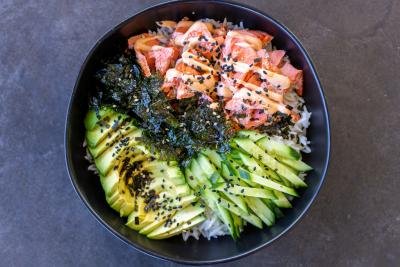Rice in a bowl with salmon, avocado, seaweed, cucumbers and sesame seeds.