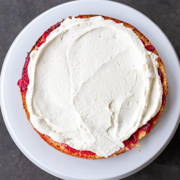 A slice of sponge cake with cranberry sauce and cream.