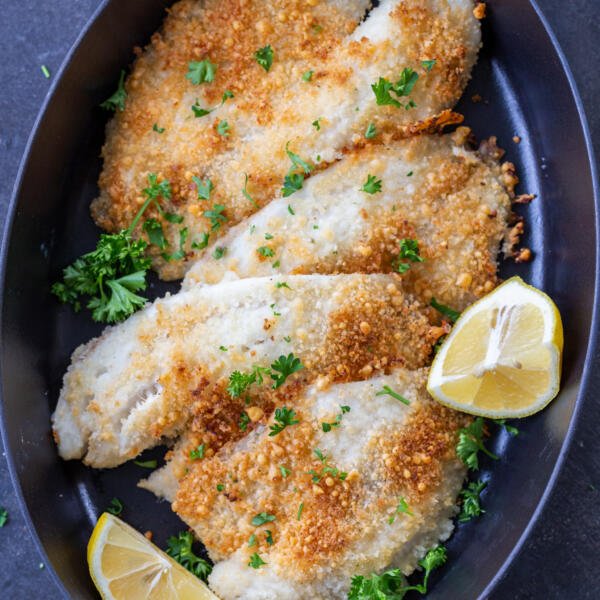 Parmesan Crusted Tilapia on a tray with herbs and lemon.