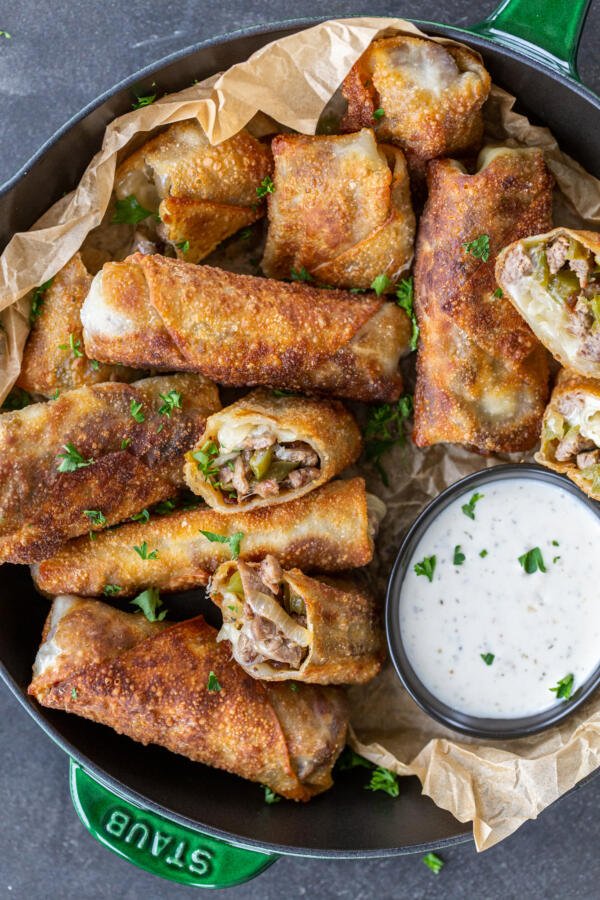 Philly Cheesesteak Egg Rolls in a serving tray with sauce. 