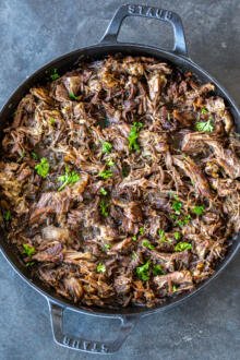 Shredded beef in a pan with herbs.