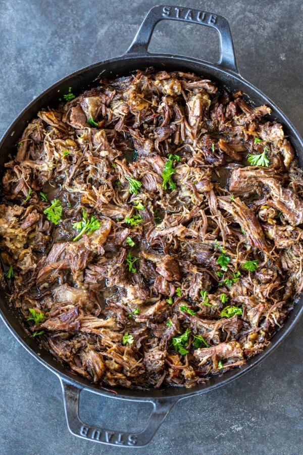 Shredded beef in a pan with herbs.