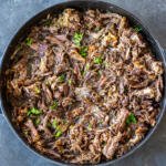 Shredded beef in a pan with herbs.