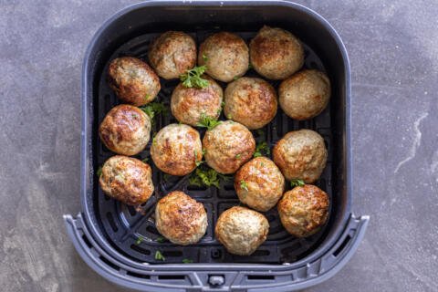 Turkey Meatballs in an air fryer basket with herbs.