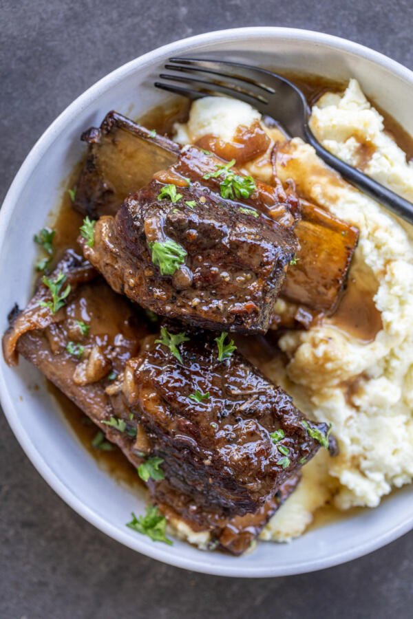 Braised beef ribs on a plate with gravy and mashed potatoes. 