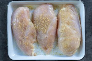 Seasoned chicken breast on a tray.