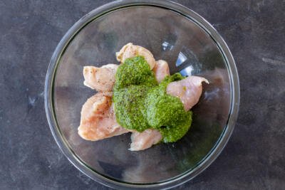 Chicken, pesto and seasoning in a bowl.
