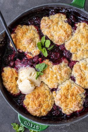 Baked blackberry cobbler in a pan with ice cream.