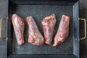 Seasoned lamb shanks on a pan.