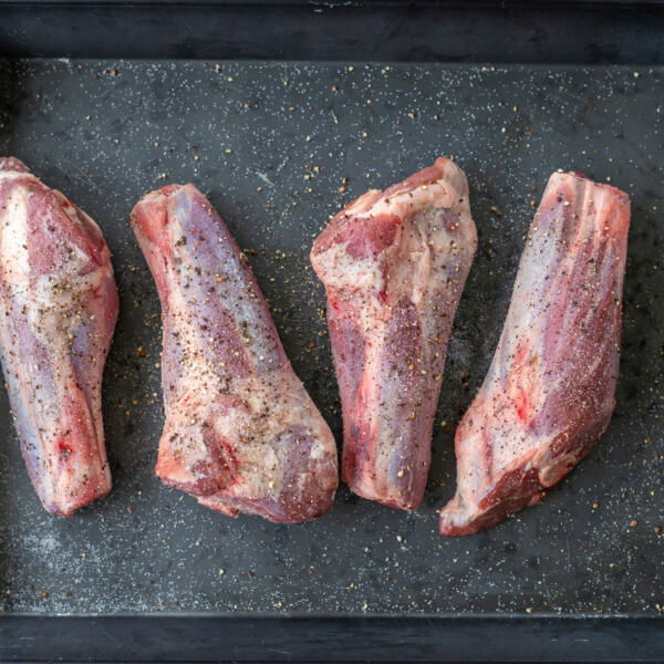 Seasoned lamb shanks on a pan.