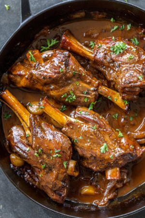 Braised Lamb Shanks in a pan with sauce.