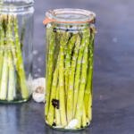 Pickled asparagus in a jar with a jar next to it.
