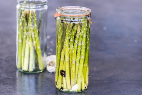 Pickled asparagus in a jar with a jar next to it.