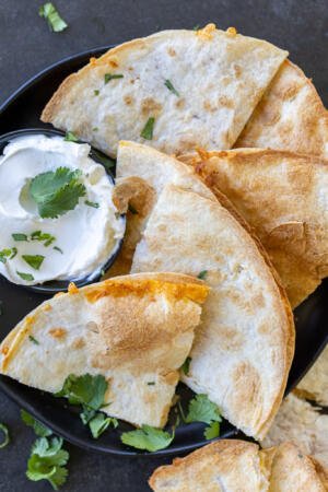 Air fryer Quesadillas in a plate with sour cream and herbs.