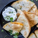 Air Fryer Quesadillas on a serving tray with sour cream and herbs.
