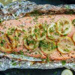 Grilled Salmon in Foil on a peice of foil on a tray with herbs and lemon.