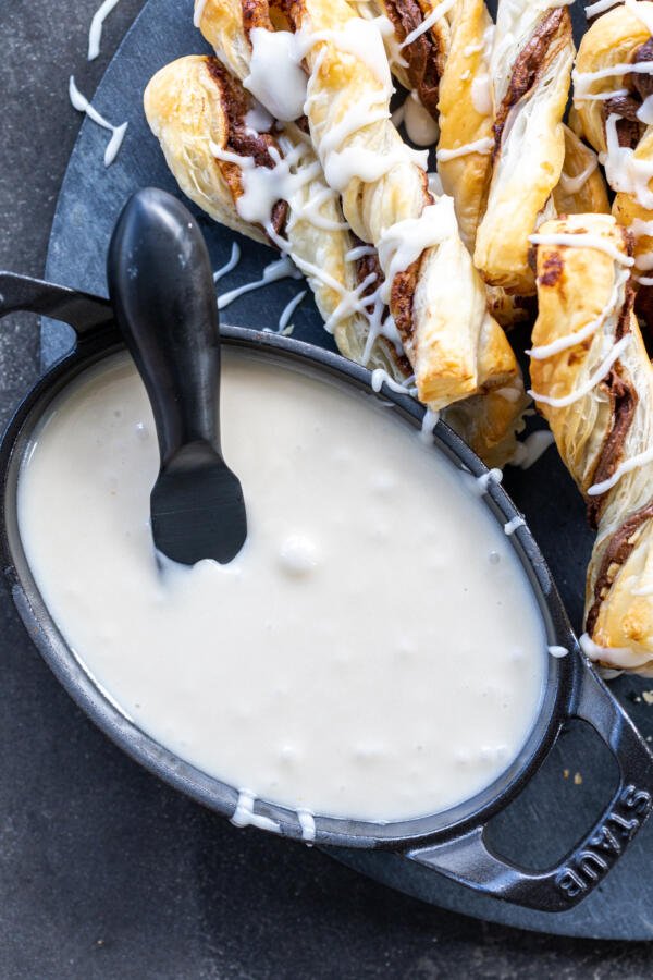 Powdered sugar glaze in a bowl with pastries next to it. 