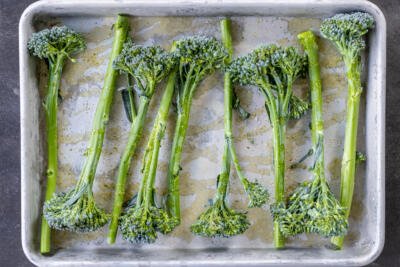 Broccolini on a pan with seasoning and oil.