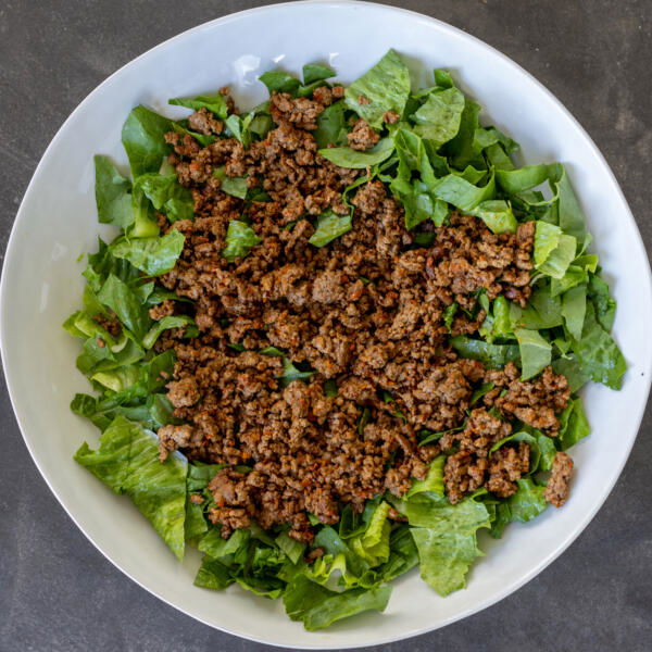 Ground beef added to the lettuce in a bowl.