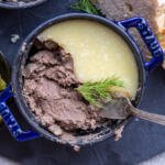 Liver pate in a pan with herbs and bread around it.