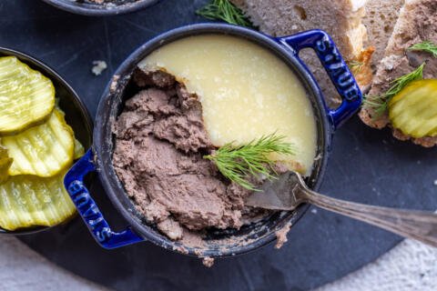 Liver pate in a pan with herbs and bread around it.