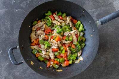 Chicken added to the veggies in a wok.