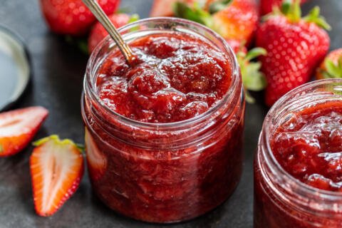 Strawberries around jar with jam.