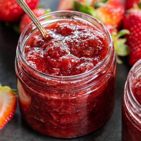 Strawberries around jar with jam.