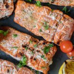Grilled salmon on a tray with herbs and veggies.